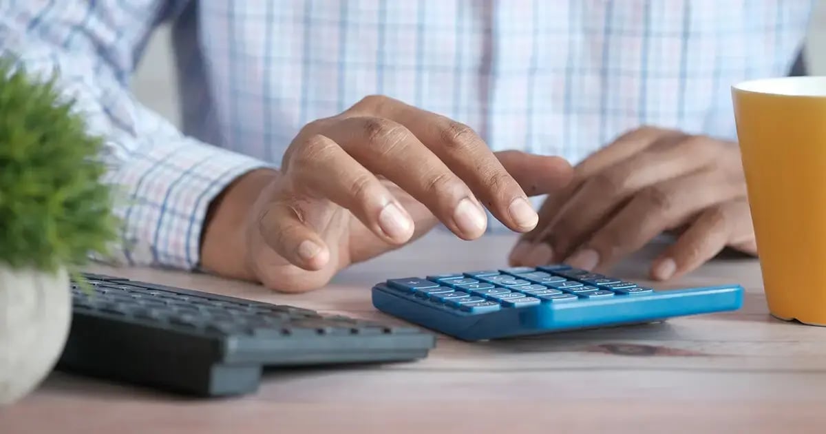 Hands of a person wearing a shirt, typing something into a calculator.