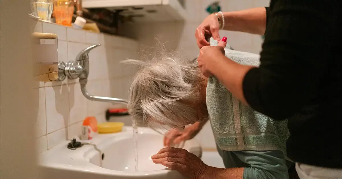 A family caregiver washes her mother’s hair at the sink.