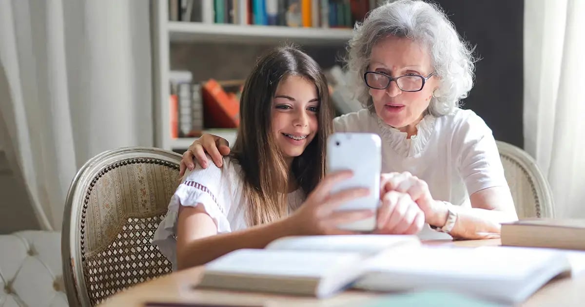 Grandchild shows their grandmother a smartphone, both are laughing.