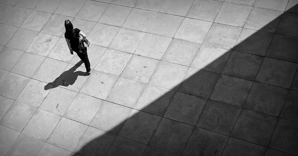 Schwarz-Weiss-Bild, das durch einen Schatten diagonal in 2 Teile geteilt wird. Im hellen Teil läuft eine Person. Symbolbild für Angststörung