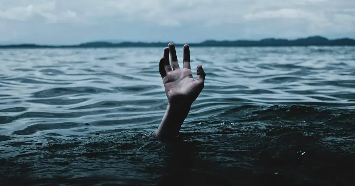 A single hand reaching out of the water, presumably in a large lake. Saturated colors. Symbolic image for burnout.