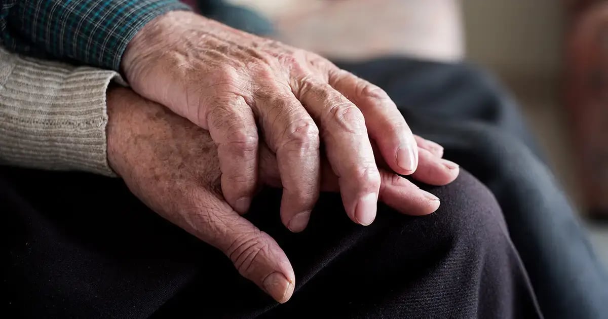 Mann hält Hand von Frau, beide alt