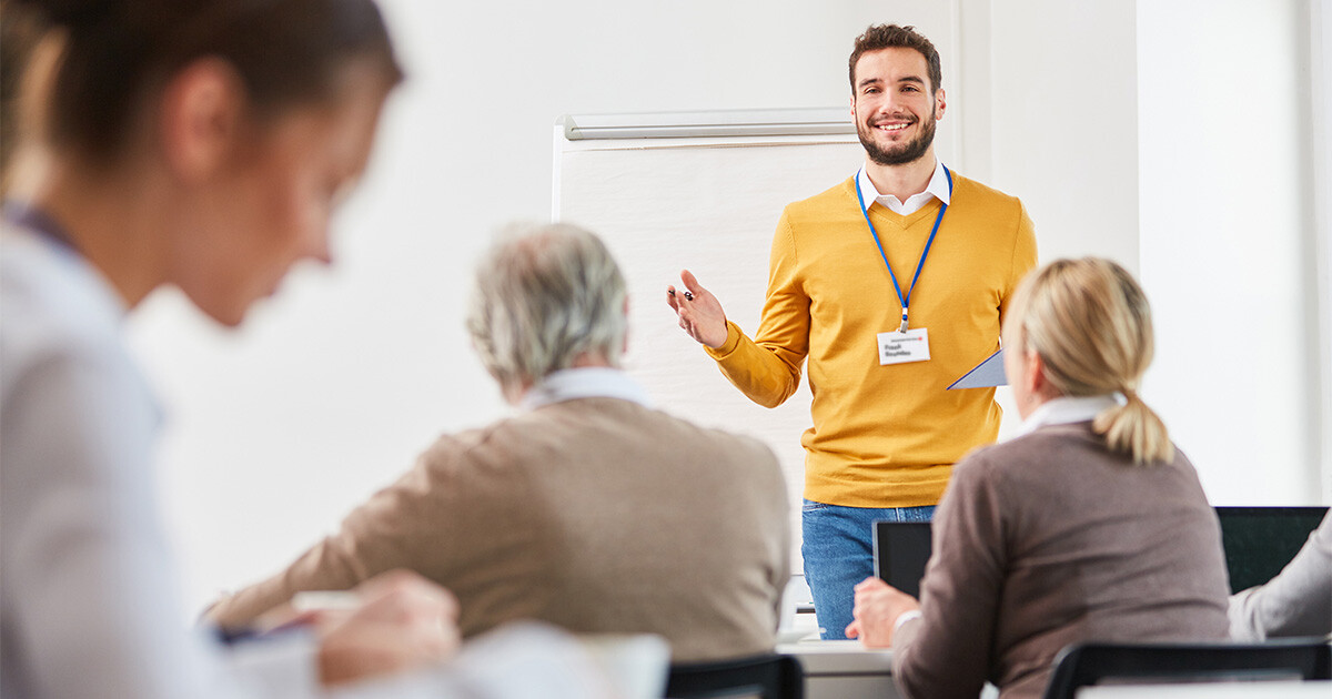 Referent steht vor einer Klasse bestehend aus unterschiedlich alten Menschen