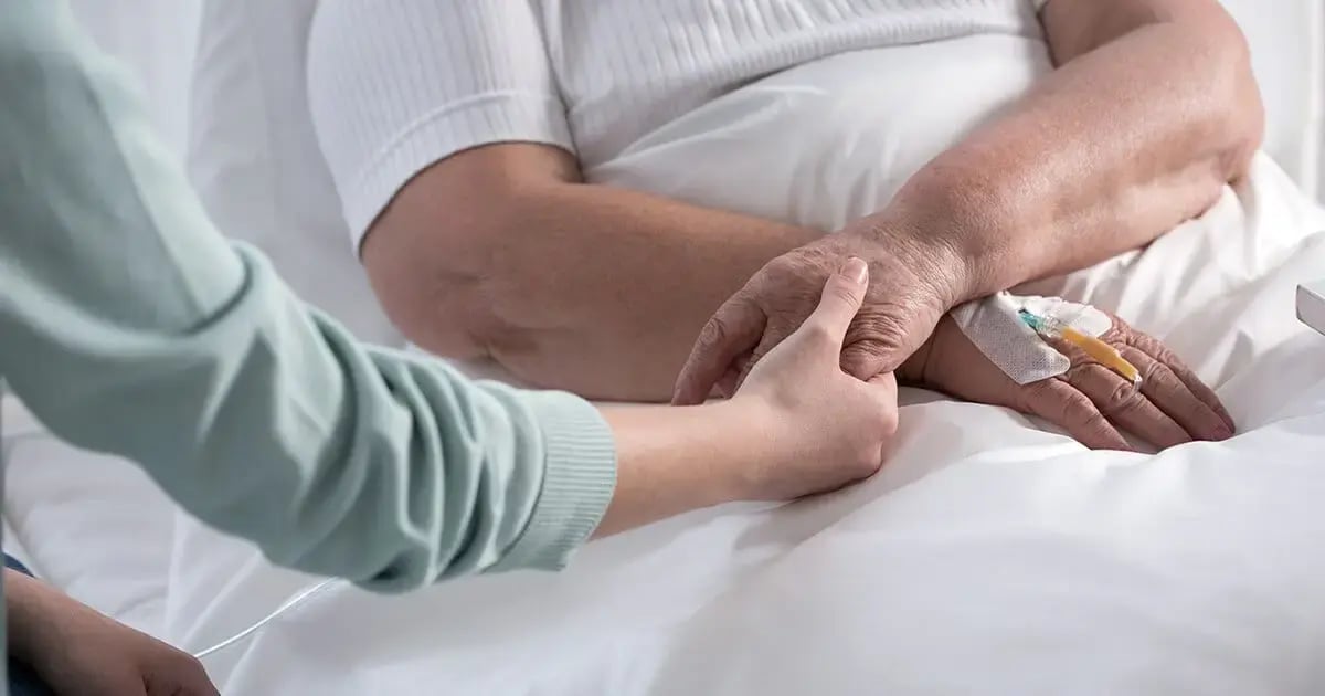 Eine Person hält tröstend die Hand einer älteren Person mit einem IV-Zugang im Bett, symbolisch für private Spitex-Dienste im häuslichen Umfeld.