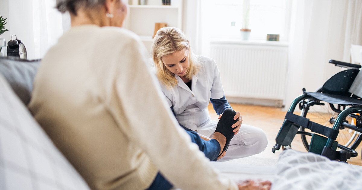 Private Spitex-Mitarbeiterin zieht älterer Patienten zu Hause Schuhe an.