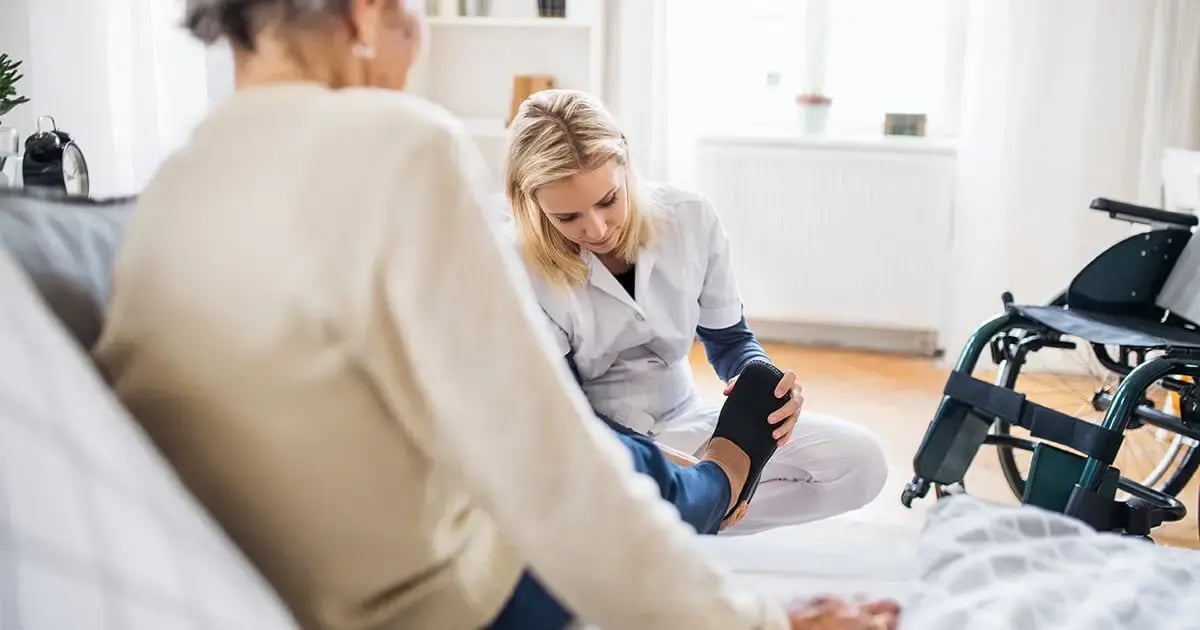 Private Spitex-Mitarbeiterin zieht älterer Patienten zu Hause Schuhe an.