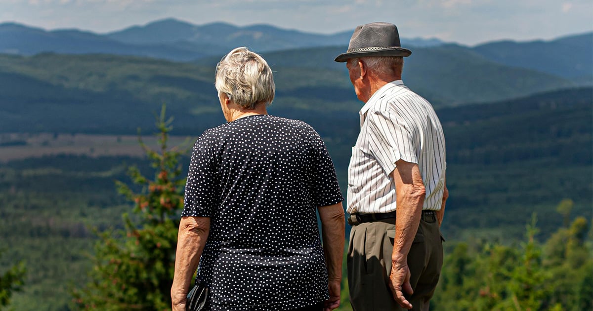 Älteres Paar betrachtet von einer Aussichtsplattform aus die malerische Landschaft der Schweizer Alpen, symbolisch für Pflegebedarf in der Schweiz