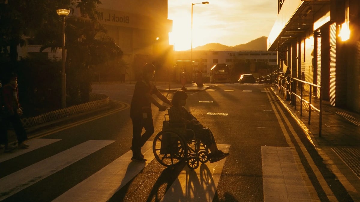 Person helps another person in a wheelchair across the road