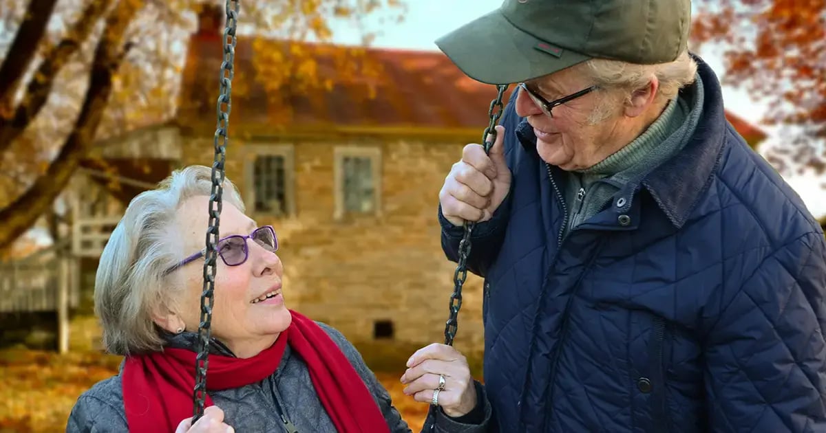 Elderly couple smiling at each other, with the woman sitting on a swing.